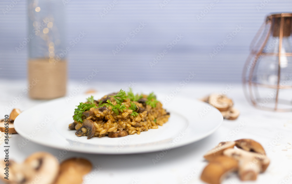 Mushroom risotto with Parmesan cheese and white Wine in a white serving plate on a white marble table with risotto Rice and raw mushroom on the side. Free space for your text/decoration.