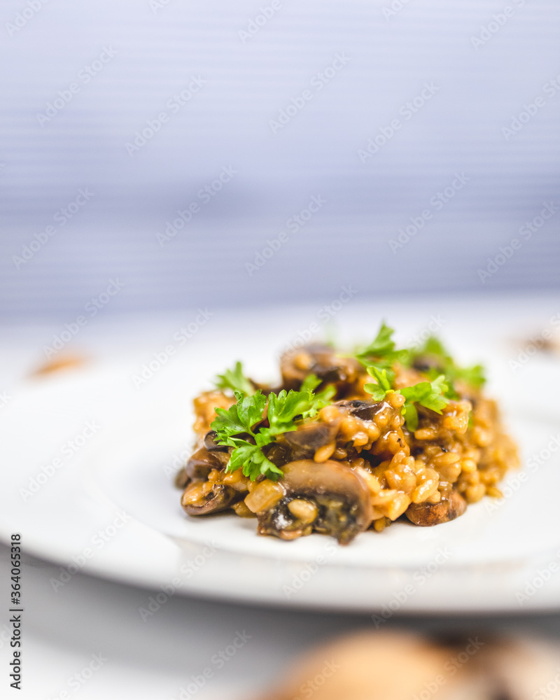 Mushroom risotto with Parmesan cheese and white Wine in a white serving plate on a white marble table with risotto Rice and raw mushroom on the side. Free space for your text/decoration. Mushroom risotto with Parmesan cheese and white Wine in a white serving plate on a white marble table with risotto Rice and raw mushroom on the side. Free space for your text/decoration.