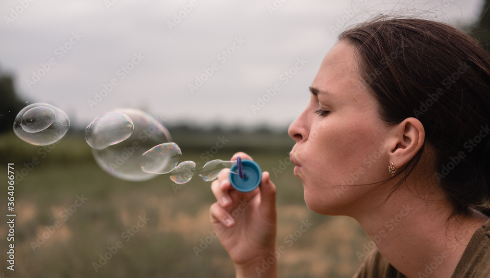 The girl blows soap bubbles. A young woman sits in nature and blows soap balls. Face in profile.