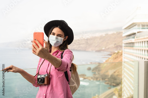 Young travel woman taking selfie with mobile smartphone wearing face surgical mask - Travel influencer having fun in vacation during corona virus outbreak - Millennial people and technology concept