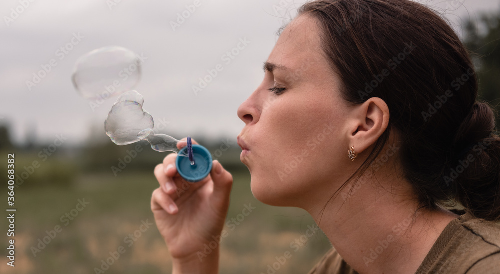 The girl blows soap bubbles. A young woman sits in nature and blows soap balls. Face in profile.