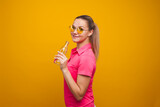 Cute blonde in sunglasses and t-shirt, drinking water from a bottle, portrait on a yellow background