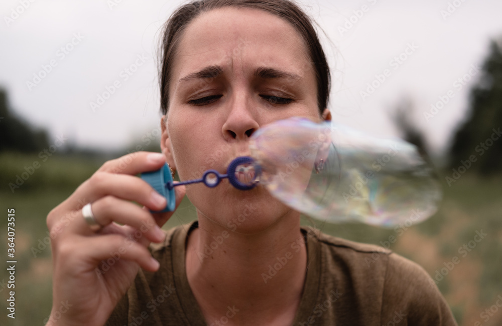 The girl blows soap bubbles. A young woman sits in nature and blows soap balls. The face in front. The girl blows soap bubbles. A young woman sits in nature and blows soap balls. The face in front.