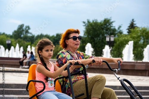 grandmother and granddaughter ride a bike in the park together