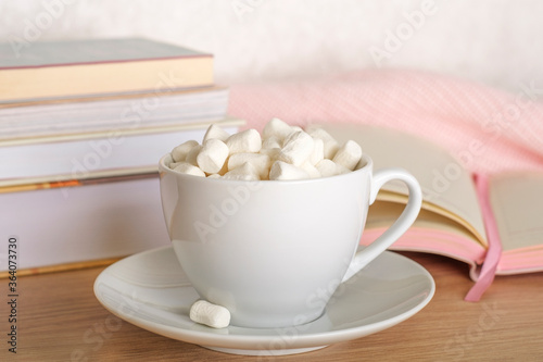 White mug of cocoa with marshmallows on the desktop. A writing desk with books, an open notebook and a marshmallow mug. 