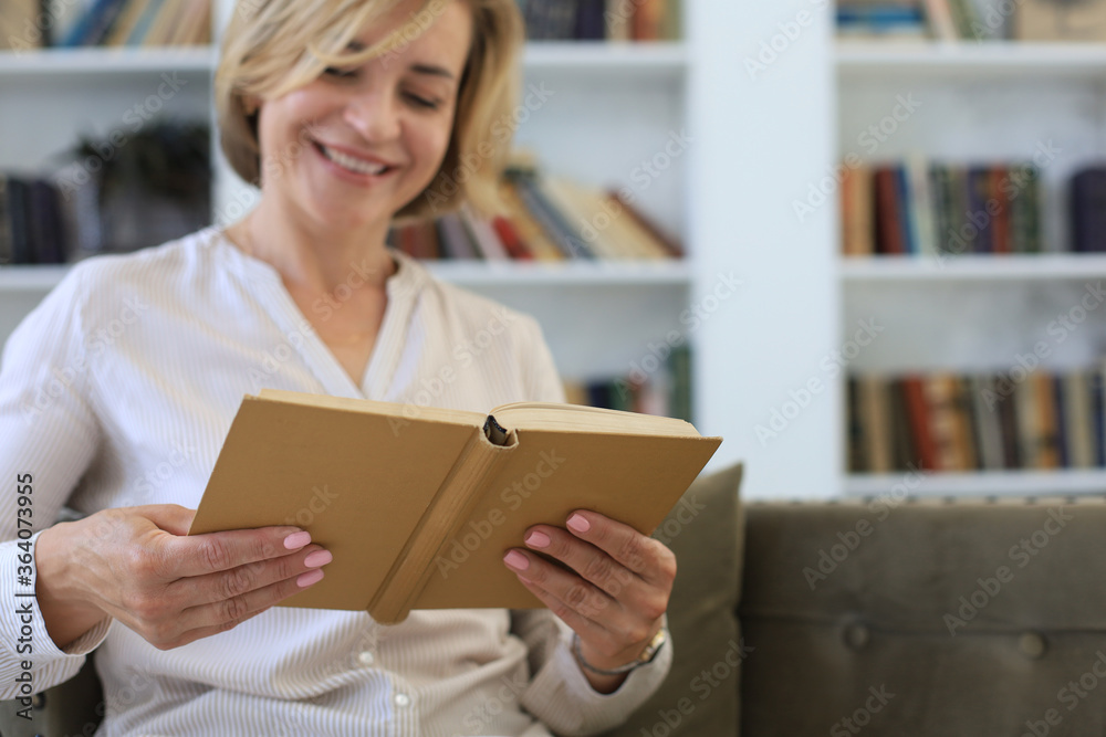 Attractive middle aged woman enjoying reading a book sitting on the sofa in her living room smiling while she reading. Attractive middle aged woman enjoying reading a book sitting on the sofa in her living room smiling while she reading.