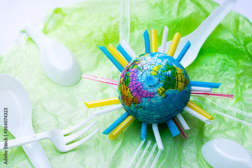 Lots of plastic waste tubes plastic bags are swallowing our world. Clean the world. The globe has a tube in middle, placed on a green crumpled plastic bag. Plastic spoons and forks flood our world. Lots of plastic waste tubes plastic bags are swallowing our world. Clean the world. The globe has a tube in middle, placed on a green crumpled plastic bag. Plastic spoons and forks flood our world.