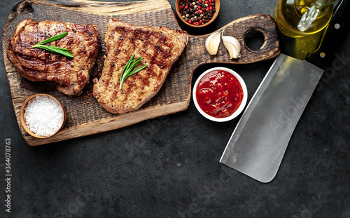 Two grilled beef steaks with spices served on a cutting board on a stone background with copy space for your text