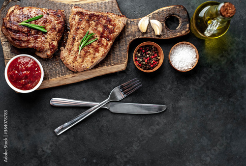 Two grilled beef steaks with spices served on a cutting board on a stone background with copy space for your text