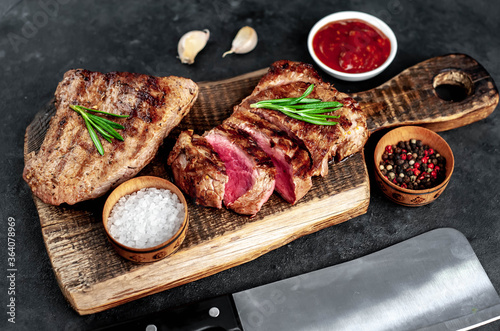Two grilled beef steaks with spices served on a cutting board on a stone background