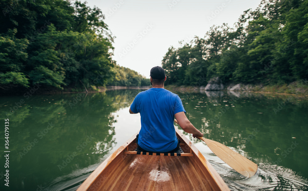 Rear view of man paddling canoe in the forest lake Rear view of man paddling canoe in the forest lake