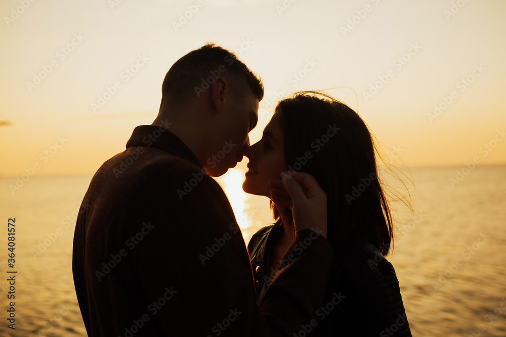 Silhouette of a close up of a woman and man standing face to face. Loving couple hugging on a sunset background. Copy space.