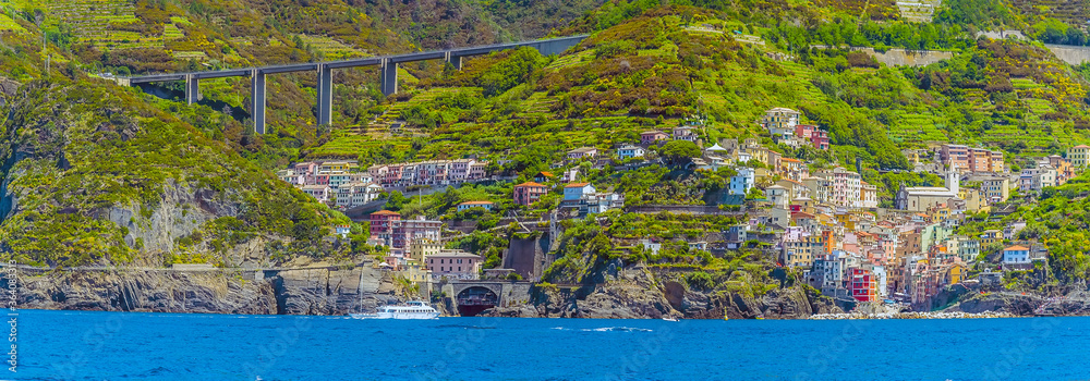 A panorama view towards the two halves of the Cinque Terre village of Riomaggiore, Italy and surrounding cliffs in summertime