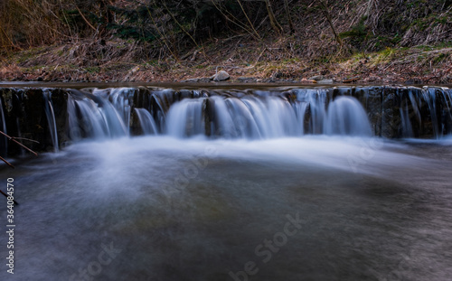 Water threshold on river Zalotomyatyi in carpatian mountains and green forest. National park Skolivski Beskidy. April 2020. Long exposure shot.