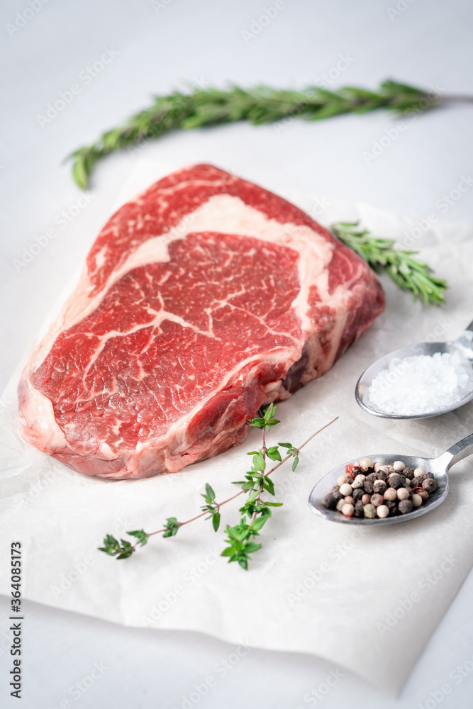 Raw rib eye steak on a light background with cooking ingredients