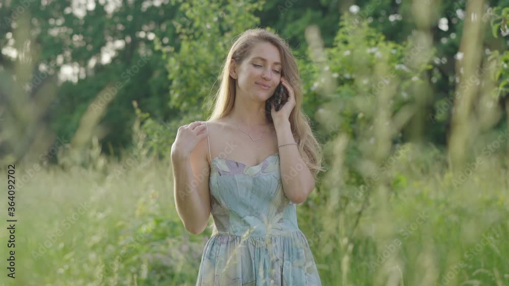 Laughing beautiful girl talking on the phone on sunny meadow. Portrait of young brunette Caucasian woman resting outdoors on summer weekend day. Leisure, relaxation, tranquility. Laughing beautiful girl talking on the phone on sunny meadow. Portrait of young brunette Caucasian woman resting outdoors on summer weekend day. Leisure, relaxation, tranquility.