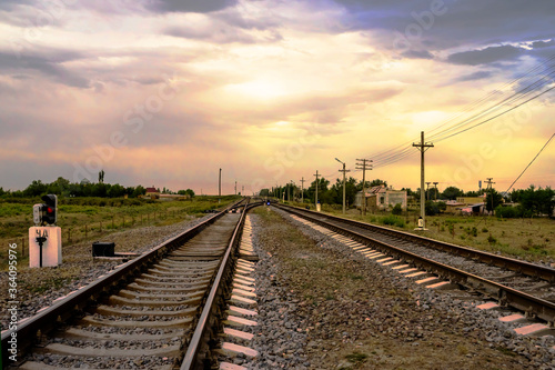 Railway at sunset. Railroad station. Railroad crossing. Railway signs at the crossroads. Sky with rain clouds at sunset. Clouds in the sky. Rails, sleepers, stones. Perspective. Horizon