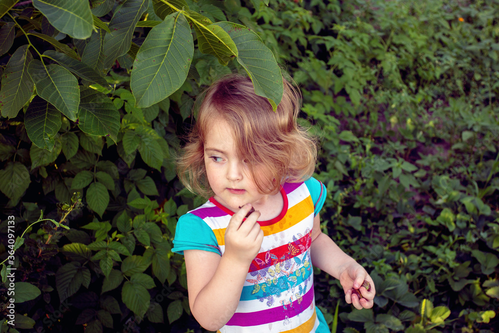 Blonde girl eating gooseberry near a green bush in a field Blonde girl eating gooseberry near a green bush in a field