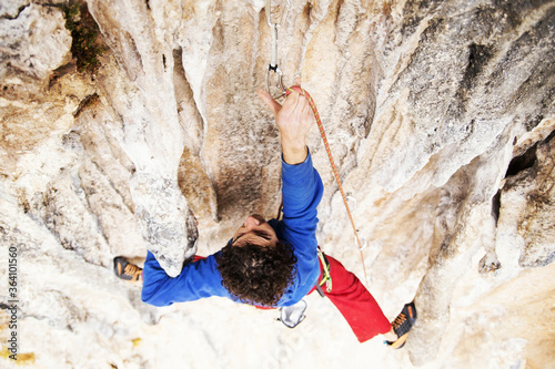Male rock climber hanging with one hand on challenging route on cliff and putting chalk on another