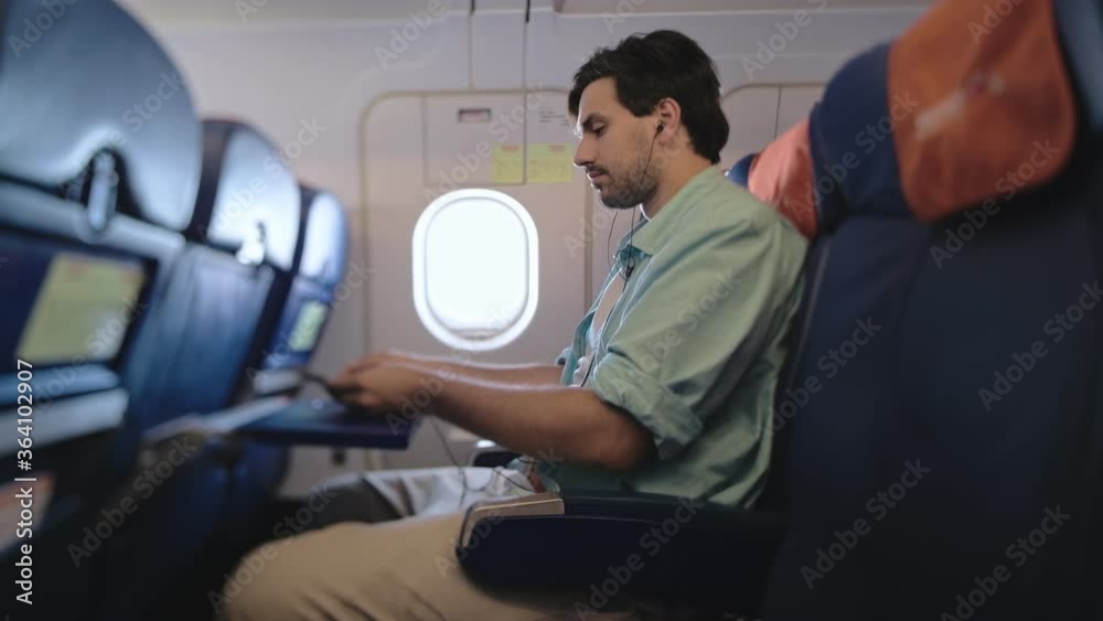 An attractive man sits alone in an airplane and holds a smartphone in his hands. Wireless technologies in civil aviation. A tourist is sitting on a sofa in an airplane. An attractive man sits alone in an airplane and holds a smartphone in his hands. Wireless technologies in civil aviation. A tourist is sitting on a sofa in an airplane.