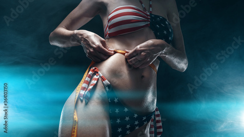woman in swimsuit american flag measures her waist in gym after workout
