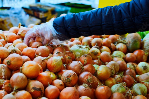 Shopper hand on yellow onions in supermarket. Yellow onions grocery store close up. Golden onions big pile on market. Woman in gloves baying fresh organic yellow onions from food supermarket shelf