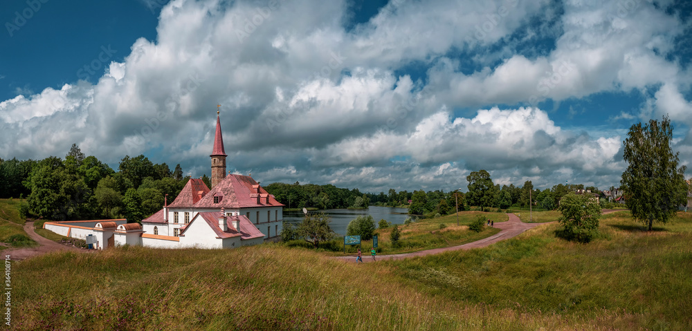 A wide panorama of the beautiful natural landscape. Old castle, blue sky and white fluffy clouds at the sunny summer day. Gatchina. Russia