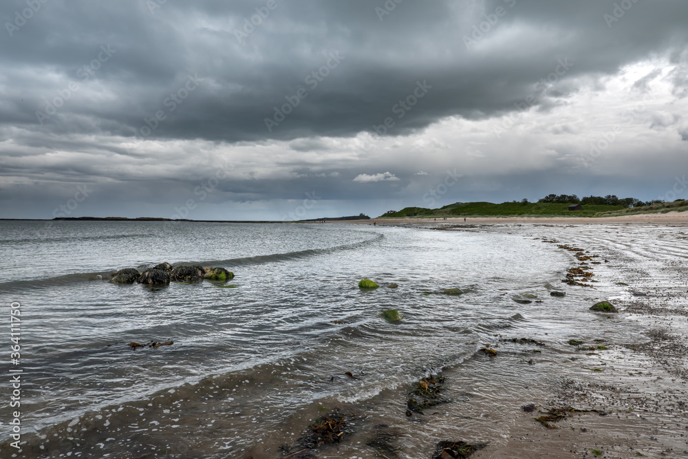 Fototapeta premium The tide has turned at Low Newton-by-the-Sea but clouds are heavy before the rain on a warm summers day.
