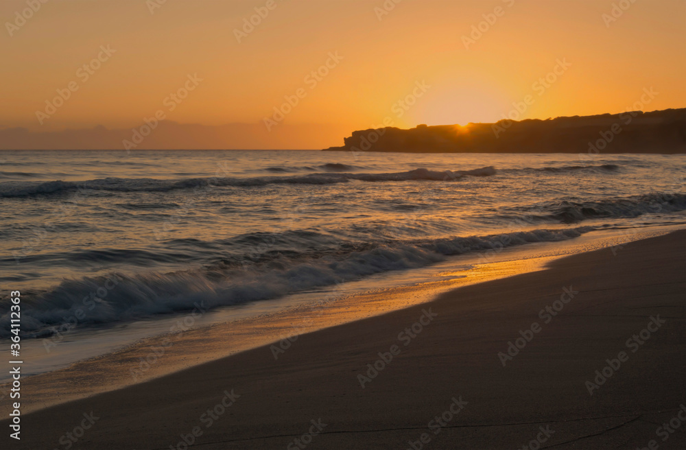 Alba sul mare con mare agitato, sabbia e scolgi sullo sfondo.