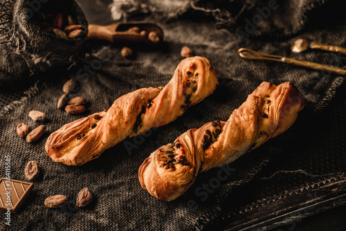 Fotografi Freshly backed twisted cakes or puff pastry buns with chocolate on rustic sackcloth background