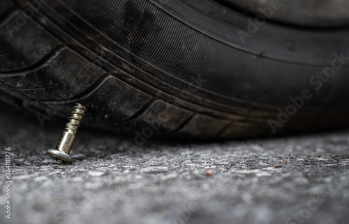 Close up button head needle metal screw nail stuck to puncture into wheel tire on the road photo