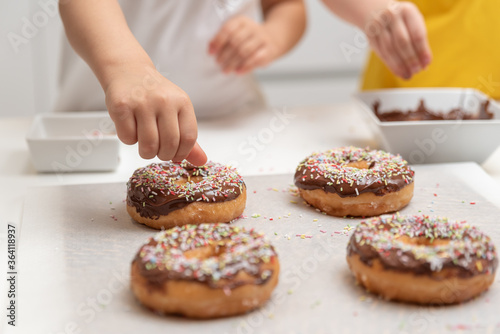 Fotografie Children decorating doughnuts with colorful sprinkles at home