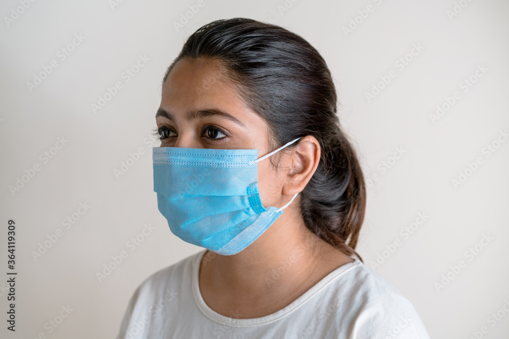 Young Indian woman wearing a protective face mask against white extendable background. Responsible, public healthcare awareness in the time of pandemic Young Indian woman wearing a protective face mask against white extendable background. Responsible, public healthcare awareness in the time of pandemic