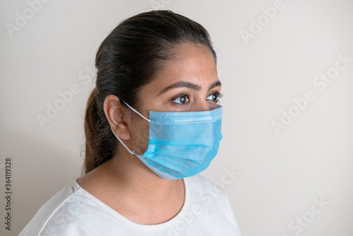 Young South Asian woman wearing a protective face mask against white extendable background - Side view. Awareness in the time of global pandemic
