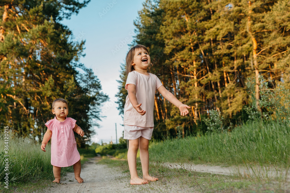 Fototapeta premium Two little sisters of Caucasian appearance play and run barefoot in nature. Concept - friendliness and family interaction between children
