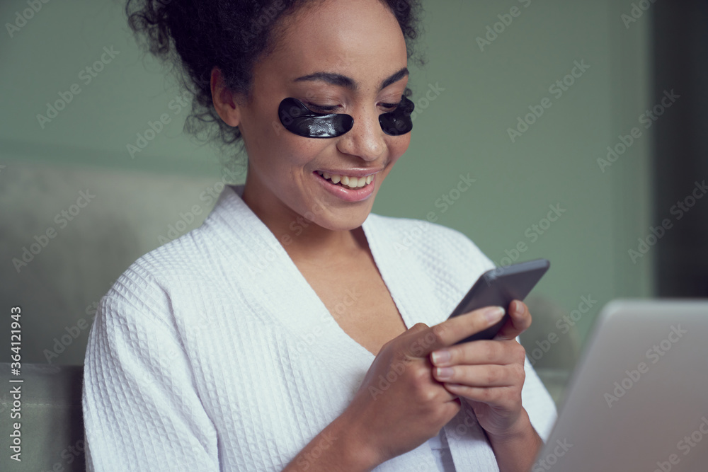Cheerful young woman relaxing with smartphone indoors