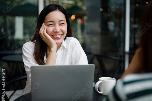 Asian woman working with computer laptop and drinking coffee in coffee shop cafe smile and happy face and talking with friend