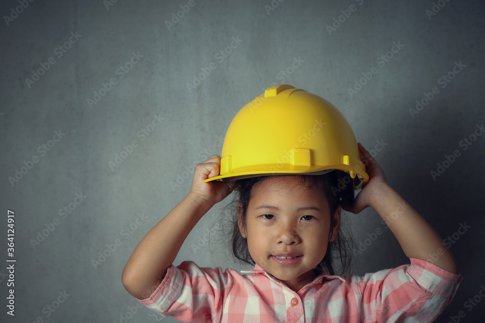 Idea and inspiration for little kids in the future. Close-up portrait Asian kid girl wearing construction helmet yellow on grey cement background with copy space. education and startup concept. Idea and inspiration for little kids in the future. Close-up portrait Asian kid girl wearing construction helmet yellow on grey cement background with copy space. education and startup concept.
