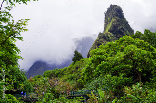 Iao Needle is a landmark rock ledge inside Iao Valley State Park with lush evergreen rainforest jungle vegetation and picturesque views of surrounding mountains and the Iao Stream river on Maui Hawaii photo