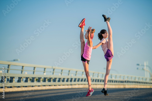 Two teenage girls perform an acrobatic element outdoors against a blue sky 