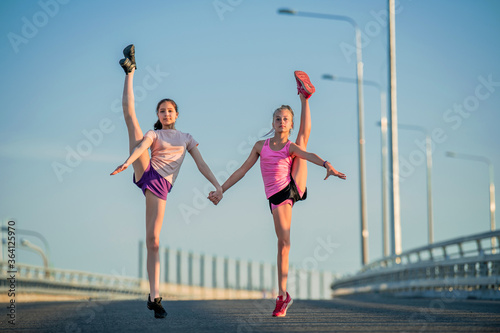 Two teenage girls perform an acrobatic element outdoors against a blue sky 