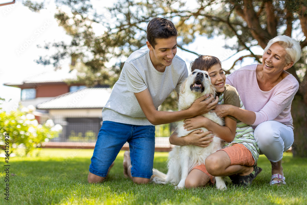 Obraz premium Mother and her sons playing with their dog in the garden 