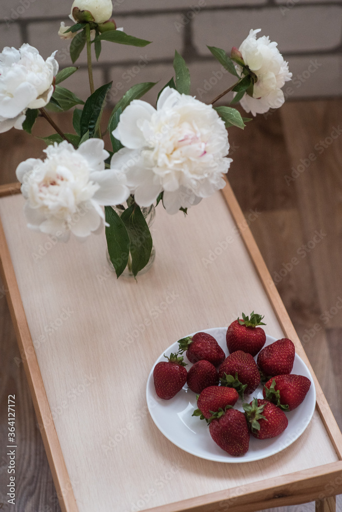 White peonies on wood table near plate of strawberryes White peonies on wood table near plate of strawberryes