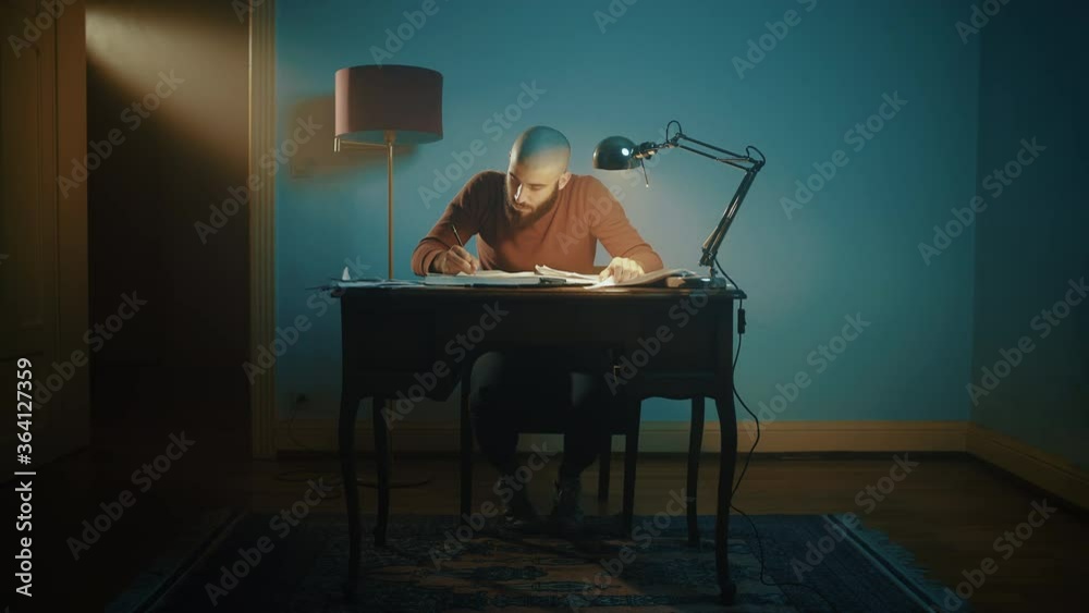 Man writing and searching for notes on a desk with a lamp