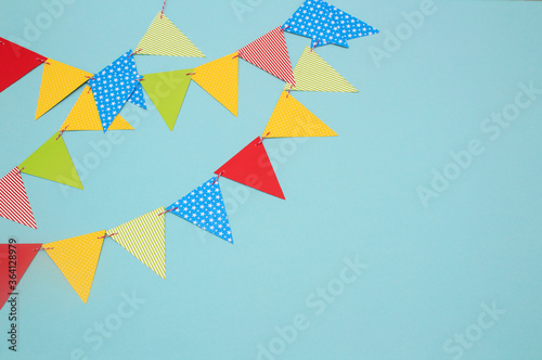 Festive garland of multi-colored paper flags on a blue background. Birthday greeting card with copy space.