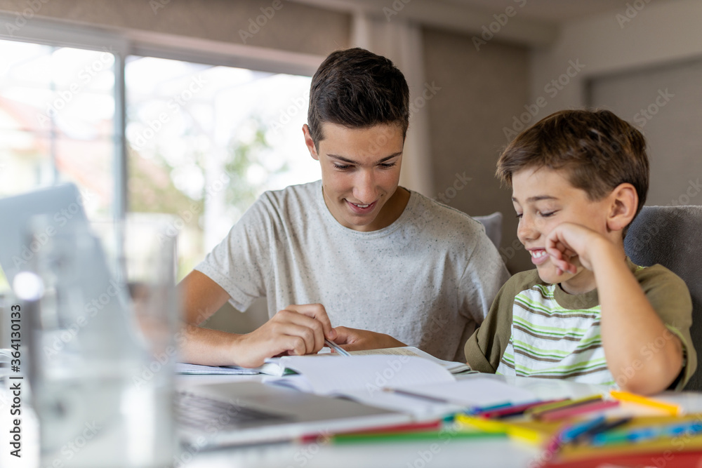 Obraz premium Teenage boy helping his younger brother doing homework at home 