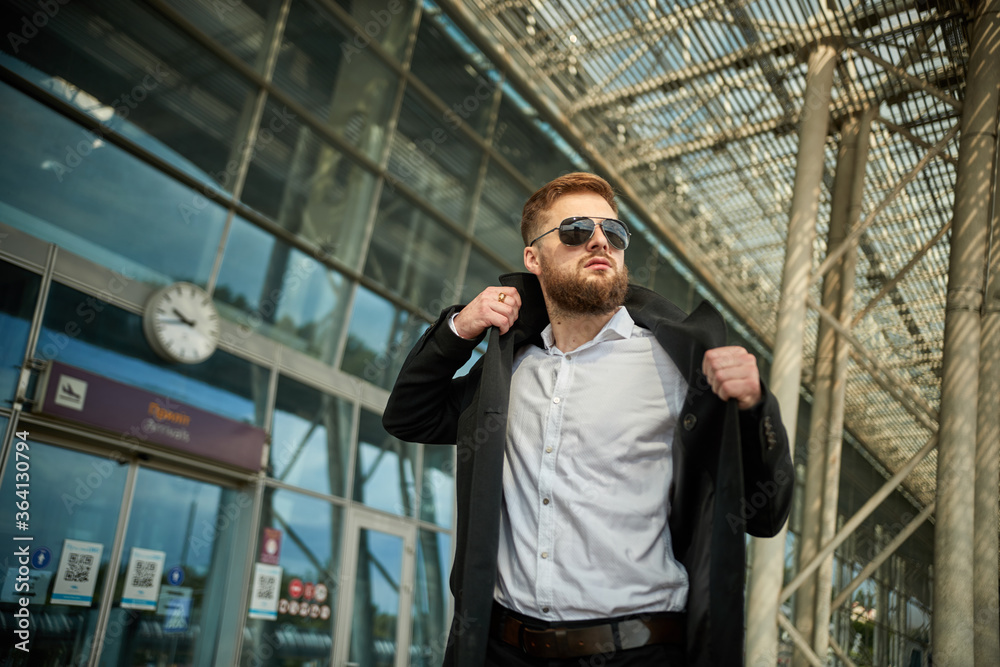 Close up of businessman putting on raincoat in city, man puts coat outside, boss or worker black suit. Serious pensive person standing sunglasses. Handsome young male office jacket. Glasses wearing Close up of businessman putting on raincoat in city, man puts coat outside, boss or worker black suit. Serious pensive person standing sunglasses. Handsome young male office jacket. Glasses wearing