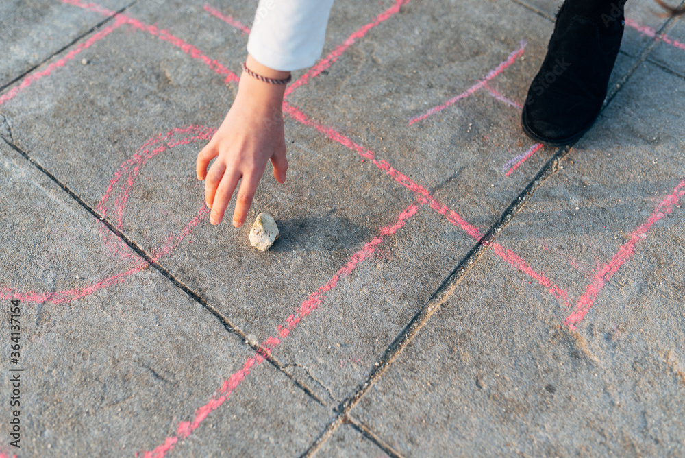 seen from above a girl's hand holding a stone while playing hopscotch in the street