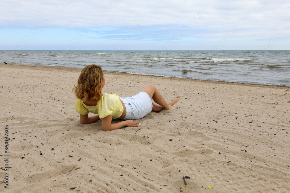 Young woman relaxing on beach. Woman taking a break to enjoy the view of the lake Young woman relaxing on beach. Woman taking a break to enjoy the view of the lake