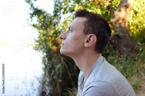 A man sits in the forest in nature and looks into the distance at the sun to sneeze.